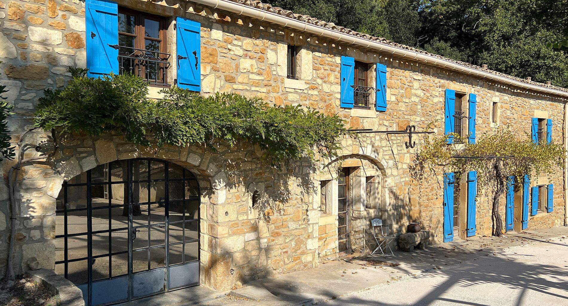 Façade en pierre du gite La Grange avec ses volets bleus et sa glycine en fleurs